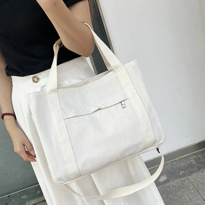 Horizontal square canvas tote bag in neutral colour with open zipper sides showing internal phone, document, computer and camera pockets