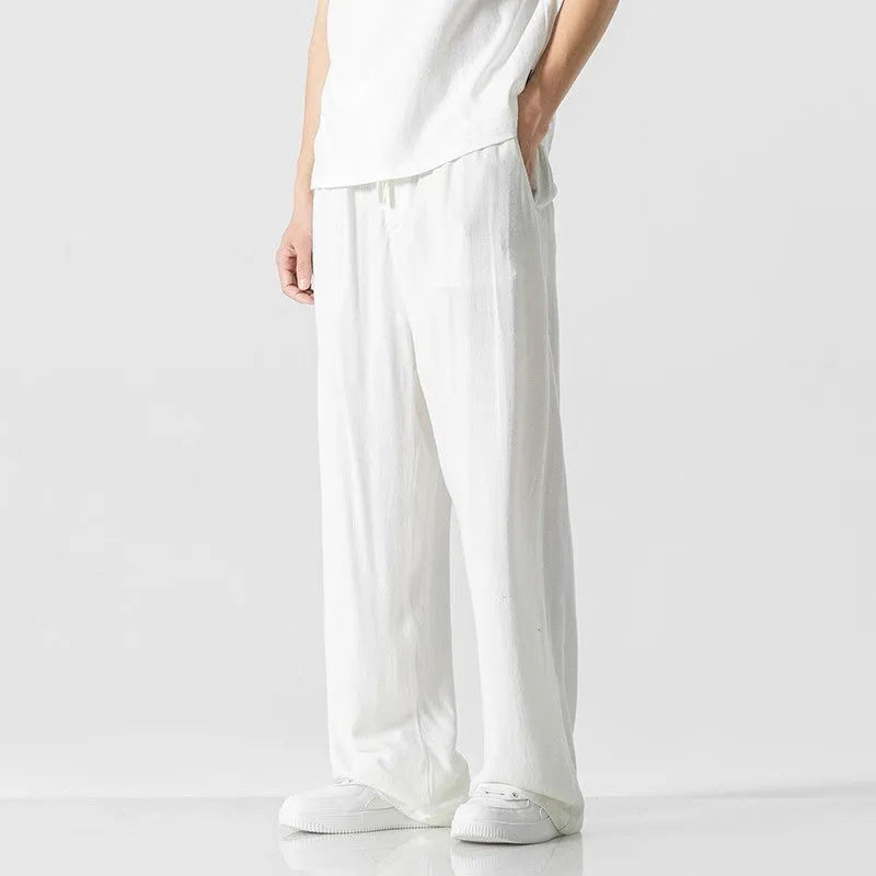 Man wearing beige straight-leg linen trousers with a drawstring waist, showcasing the cropped length and casual fit.