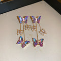 Women's silver needle coloured drop earrings with purple butterfly charm, crystal flowers, and tassels.