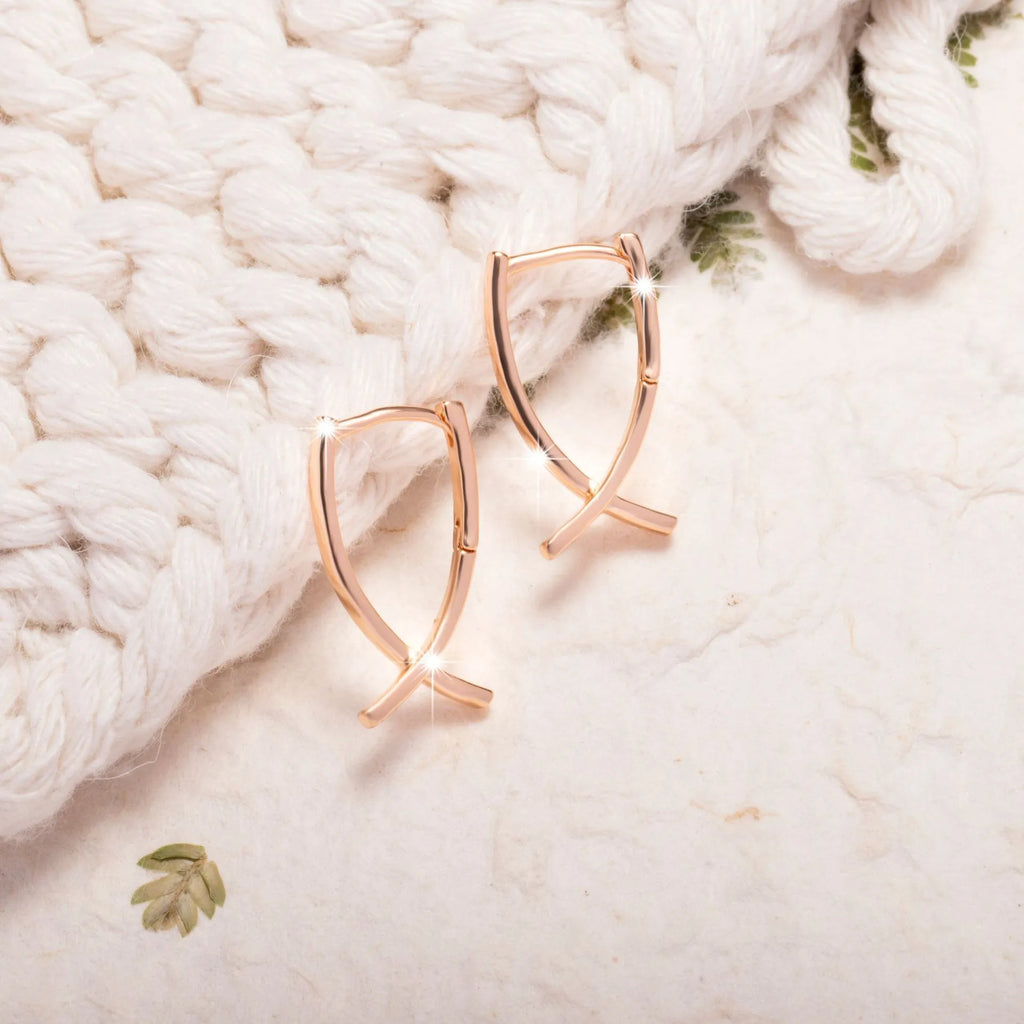 A pair of rose gold coloured cross pendant earrings on a copper base.