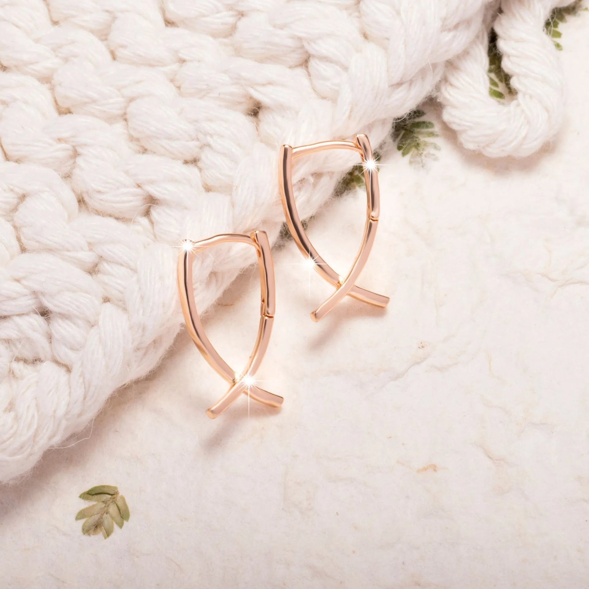 A pair of rose gold coloured cross pendant earrings on a copper base.