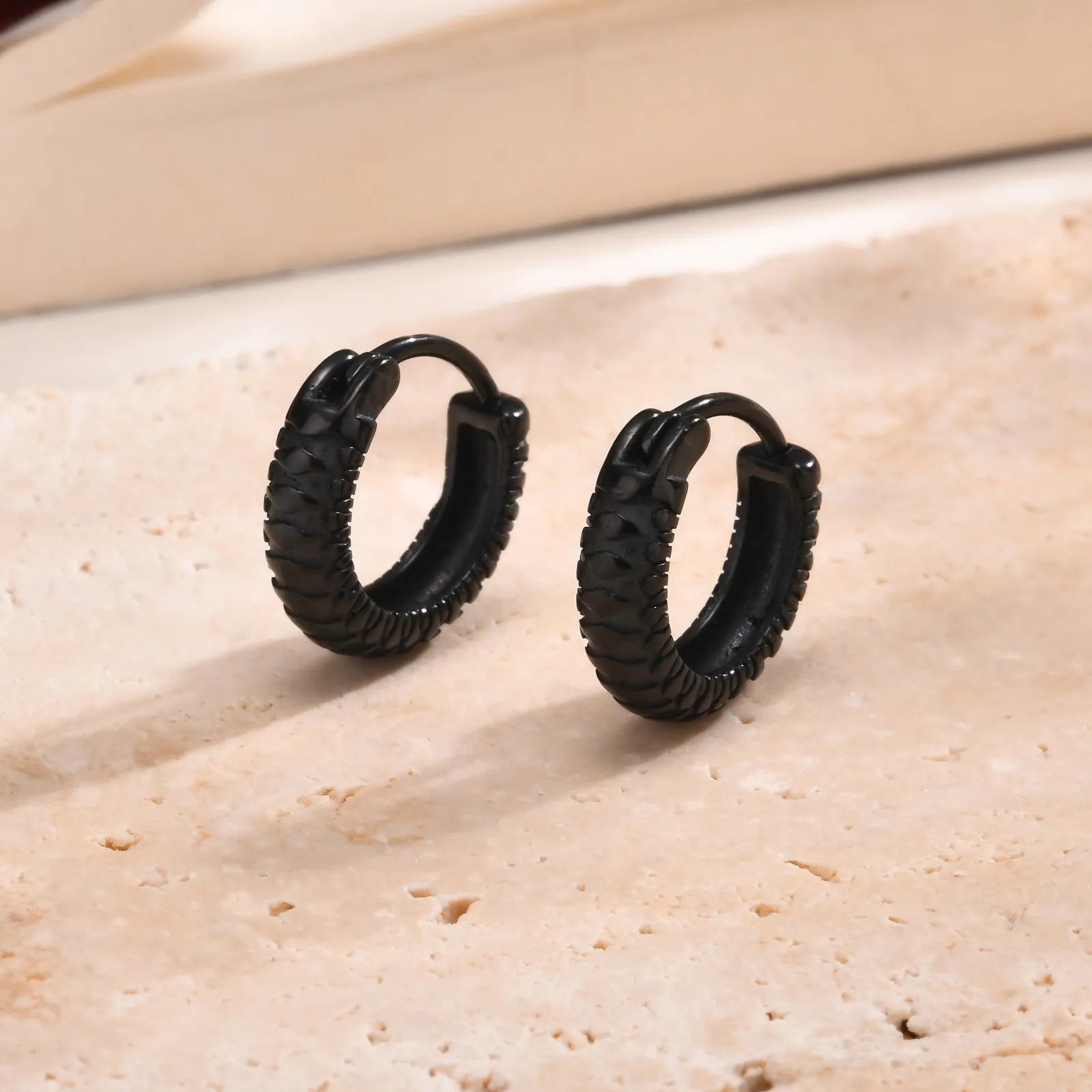 A pair of stainless steel earrings with a snake pattern design in a black finish.