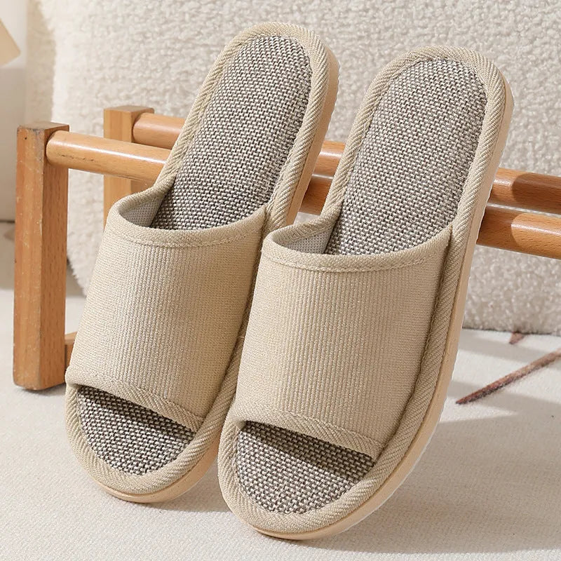 Women's open-toe linen slippers in light brown on a wooden floor, showing the breathable design and thickened sole.