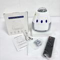 Tall white space capsule galaxy projection lamp with USB cable and remote control on a table.