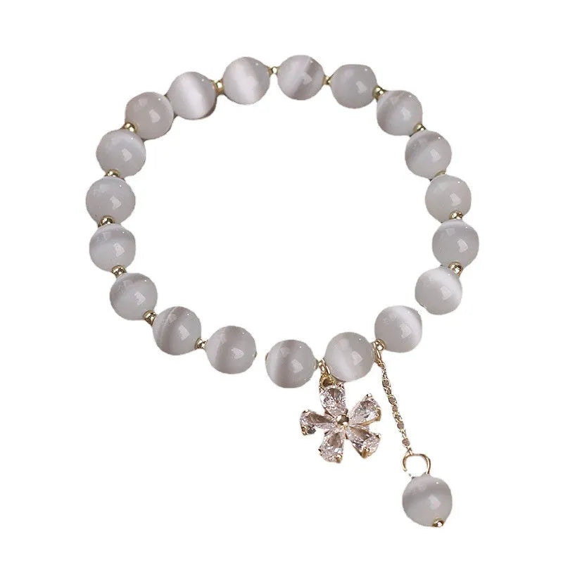 White cat's eye stone bracelet with small flower charms, tassel pendant, and safety buckle clasp.