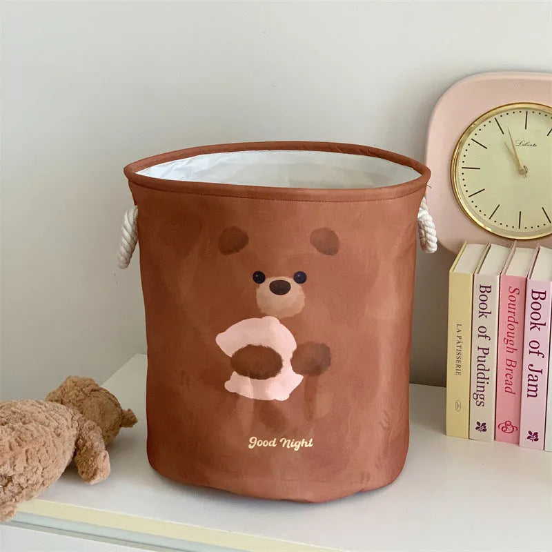 Foldable cotton laundry basket featuring an illustrated design, shown in a bedroom setting.