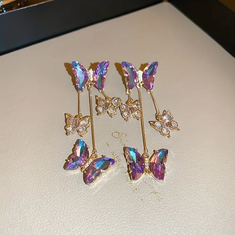 Women's silver needle coloured drop earrings with purple butterfly charm, crystal flowers, and tassels.