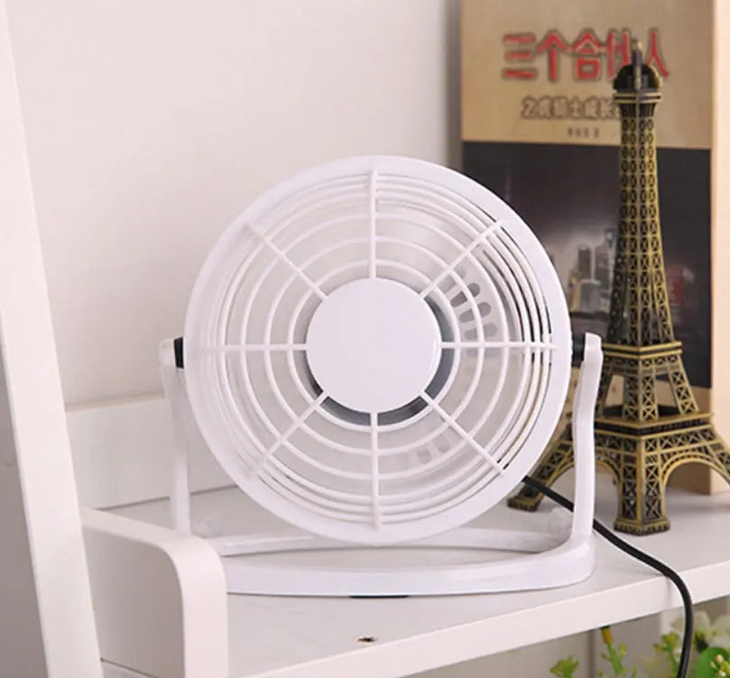 Small black USB desk fan with adjustable head and key switch on a wooden desk.