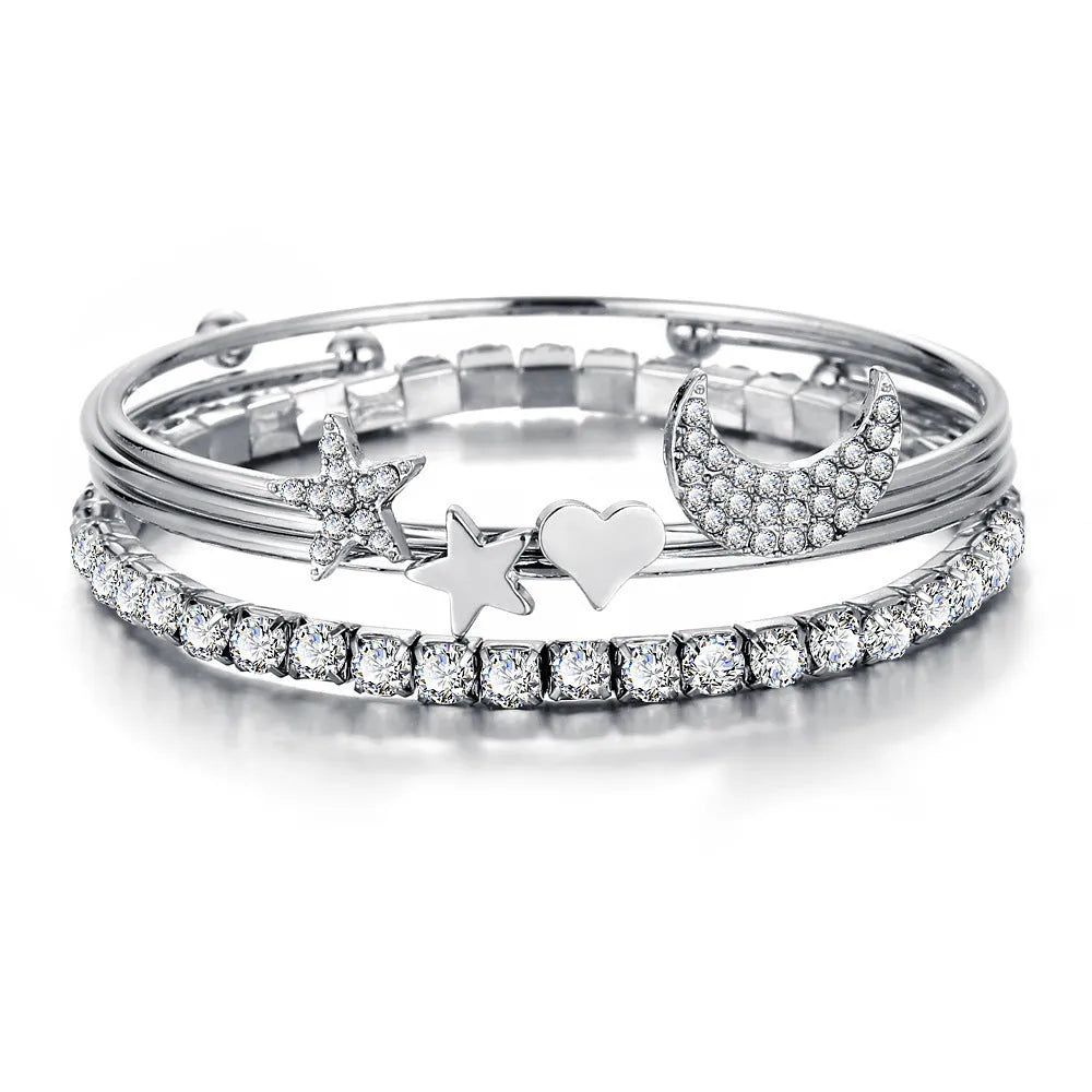 Four gold and silver metal cuff bracelets with moon and star designs on a plain background