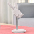 Silicone rabbit phone stand in pink on a desk holding a smartphone at an adjustable angle