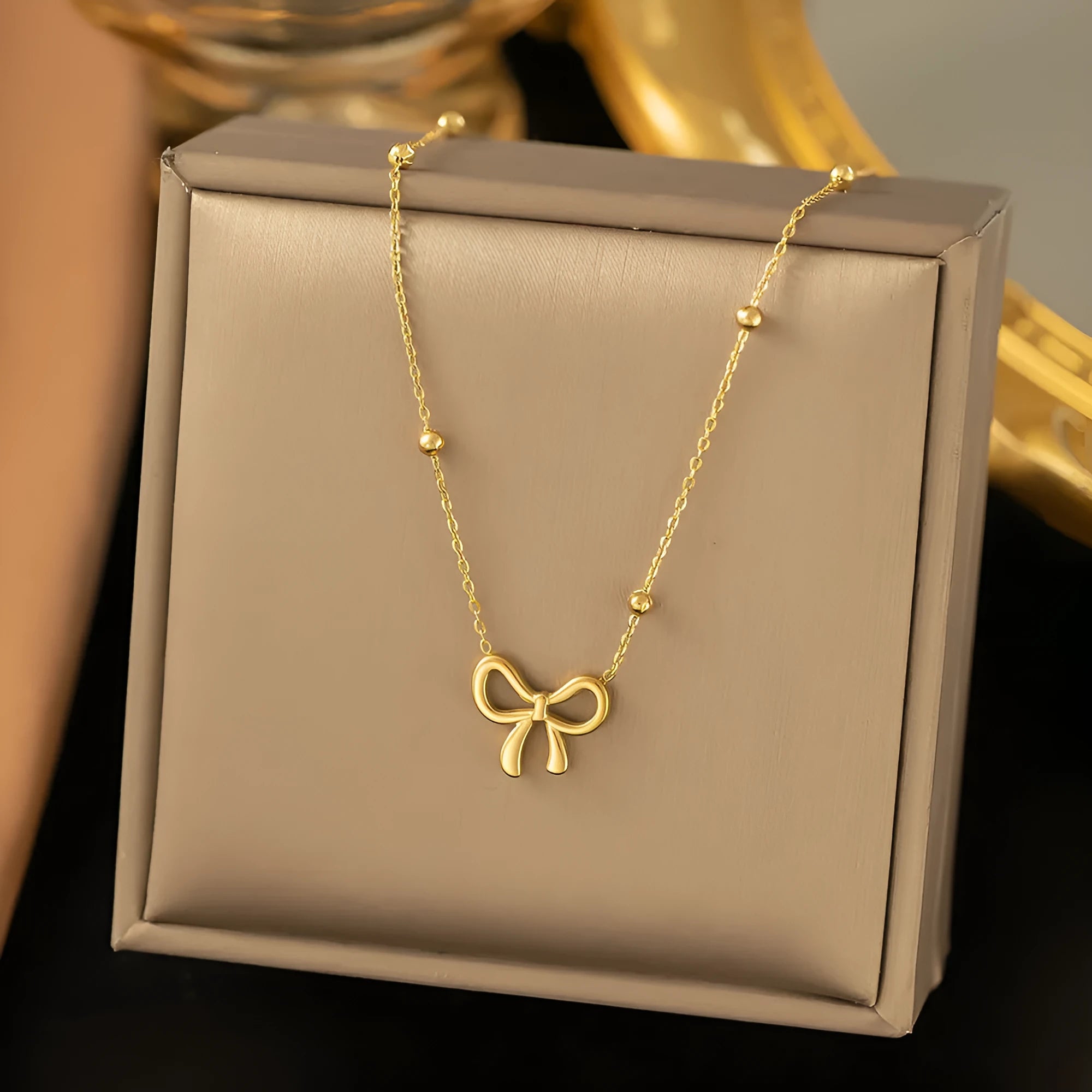Gold electroplated titanium steel bow necklace on a cross chain, adjustable length.