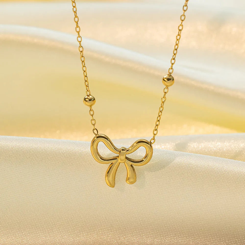 Gold electroplated titanium steel bow necklace on a cross chain, adjustable length.