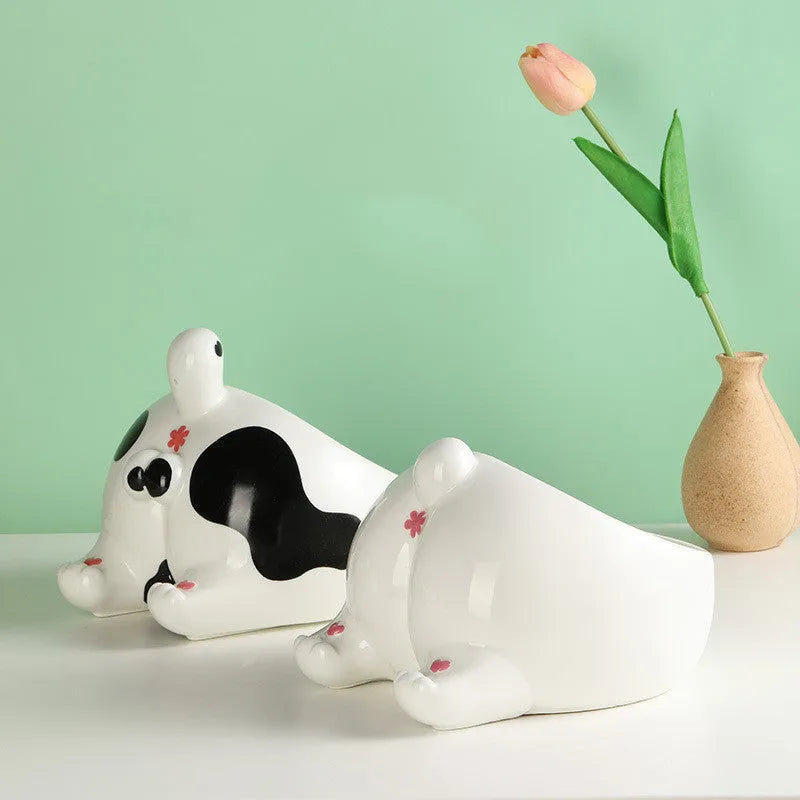 Ceramic pet bowl with inclined mouth and cartoon cat butt design, in white, on a wooden floor.