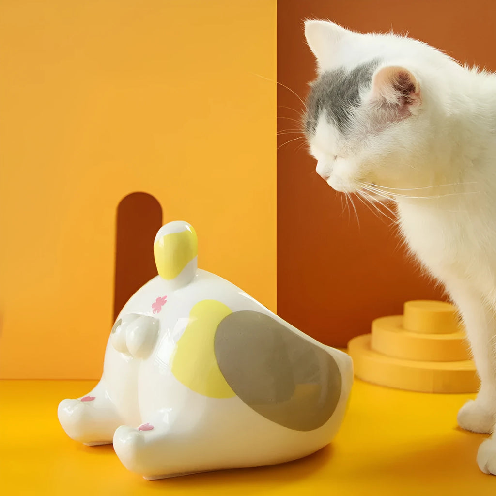Ceramic pet bowl with inclined mouth and cartoon cat butt design, in white, on a wooden floor.