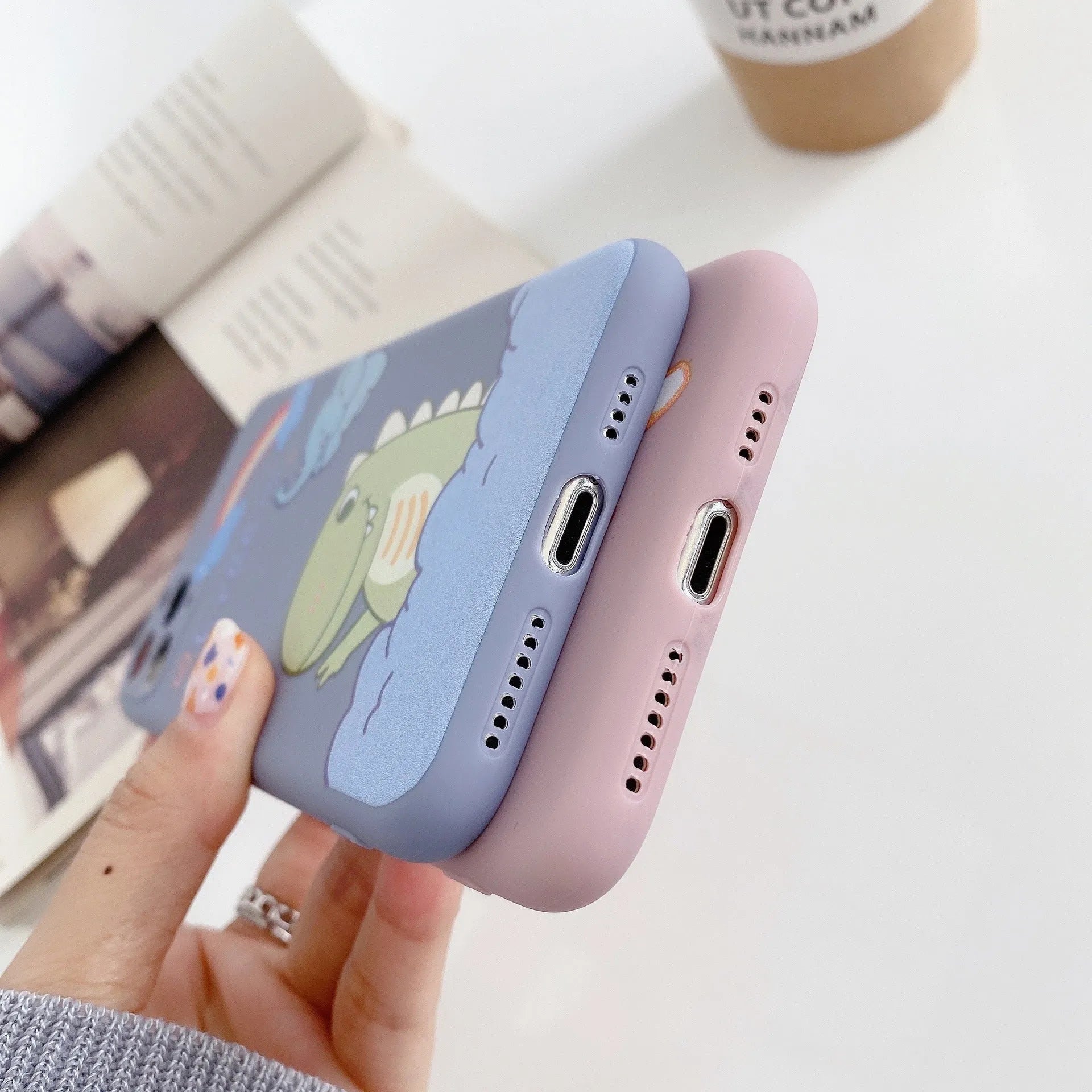 Blue soft shell iPhone case with printed cartoon dinosaur design, shown next to a pink version with a cat girl print.