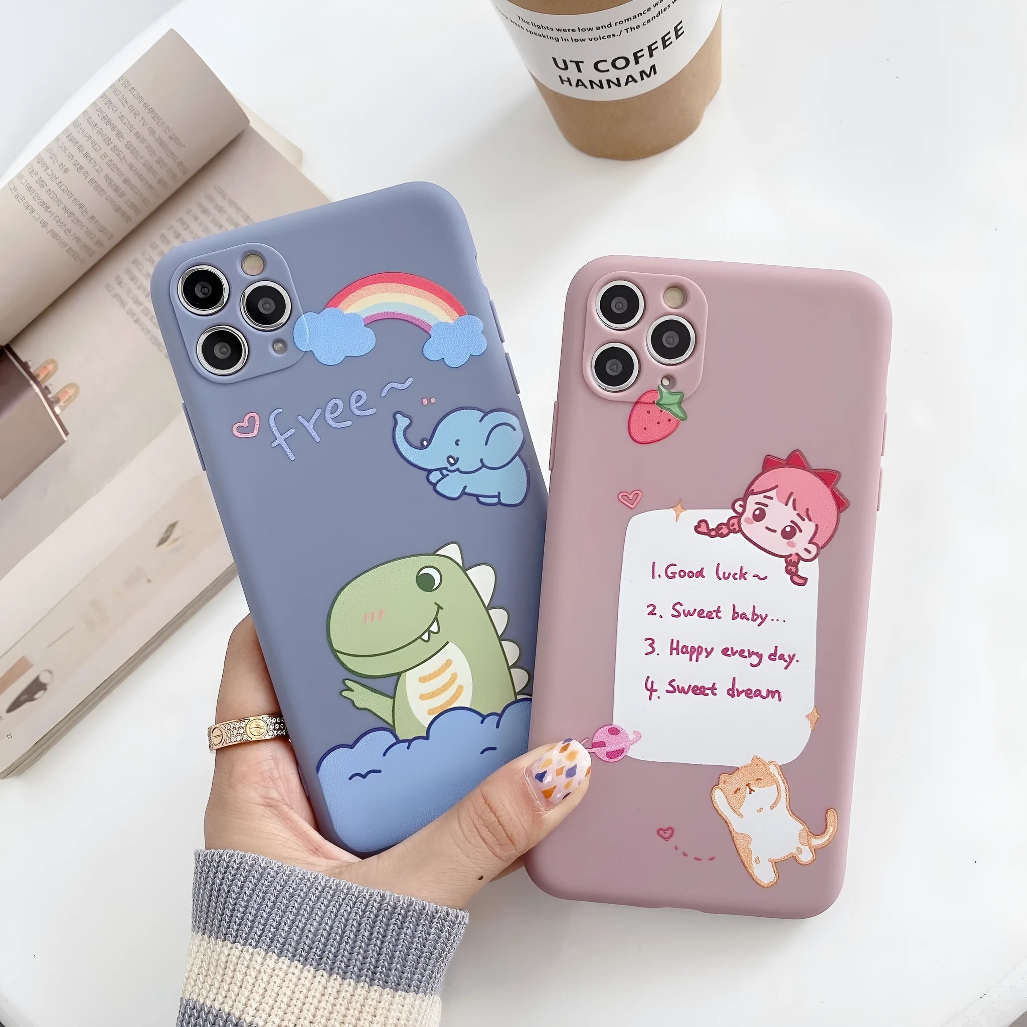 Blue soft shell iPhone case with printed cartoon dinosaur design, shown next to a pink version with a cat girl print.