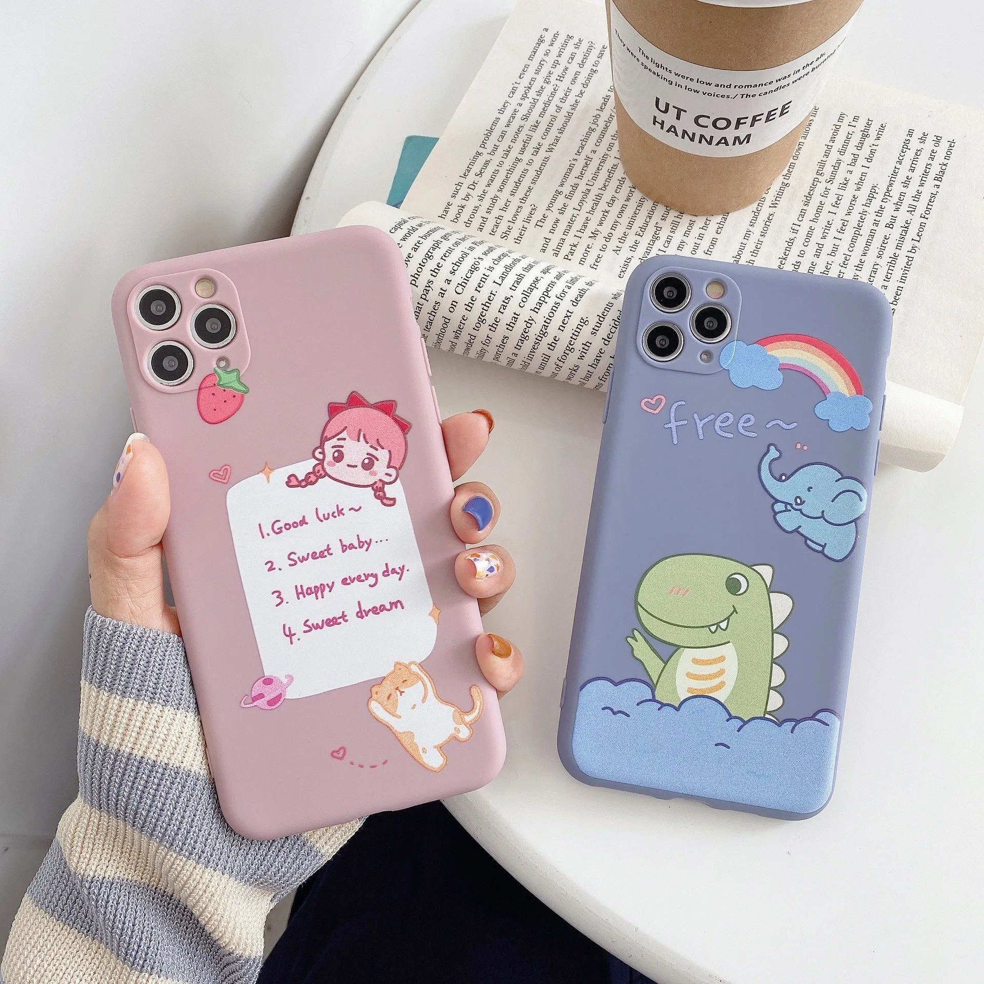Blue soft shell iPhone case with printed cartoon dinosaur design, shown next to a pink version with a cat girl print.