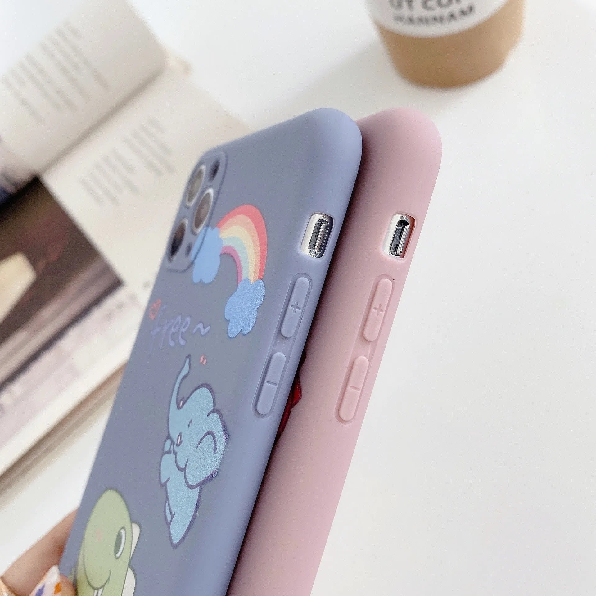 Blue soft shell iPhone case with printed cartoon dinosaur design, shown next to a pink version with a cat girl print.