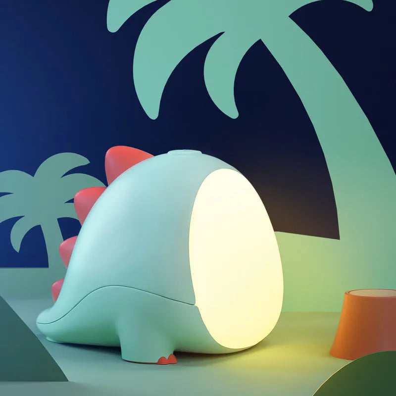 Green dinosaur silicone night light with USB charging cable on a bedside table