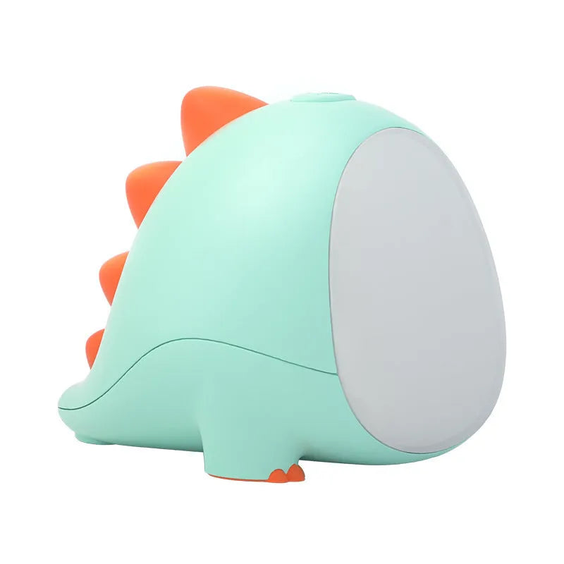 Green dinosaur silicone night light with USB charging cable on a bedside table