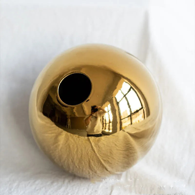 Handmade spherical ceramic vase with electroplated gold finish on a table