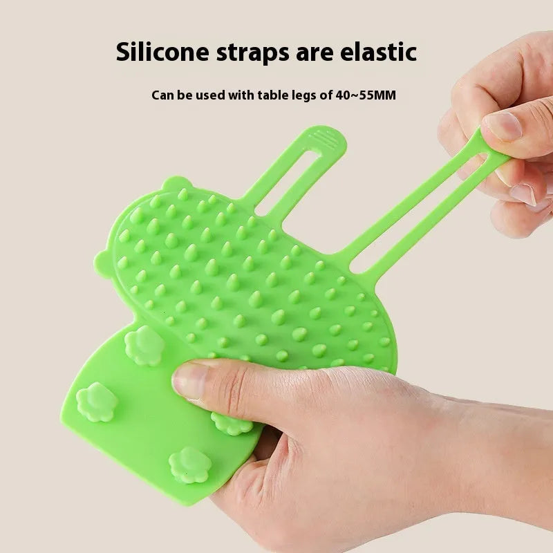 Silicone cat grooming massage comb with adjustable strap mounted on furniture leg