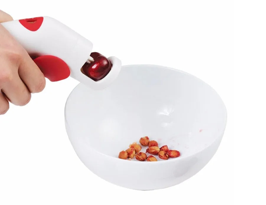 Manual cherry pitter tool with stainless steel coring mechanism on a kitchen worktop.