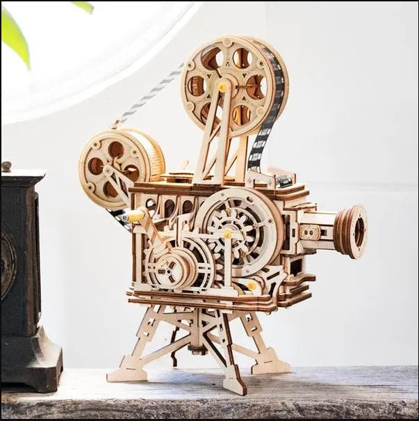 Flat-packed wooden 3D puzzle film projector with visible gear wheel assembly and hand crank