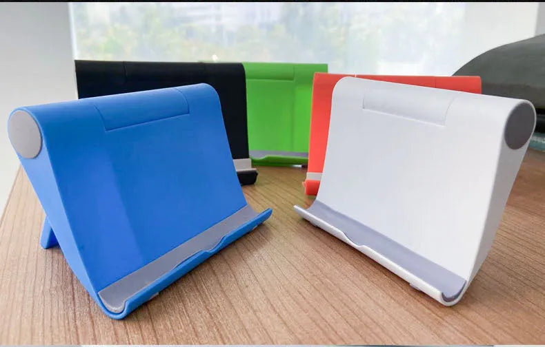 Black foldable PE plastic phone and tablet stand on a desktop, showing adjustable viewing angles.