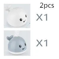 Automatic electric whale bath toy spraying water with LED lights on, floating in a baby bath.