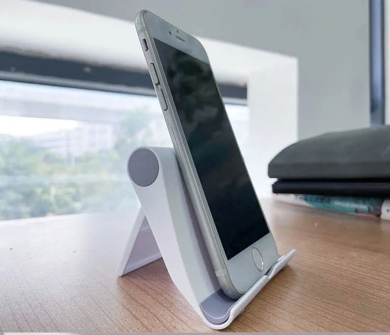 Black foldable PE plastic phone and tablet stand on a desktop, showing adjustable viewing angles.