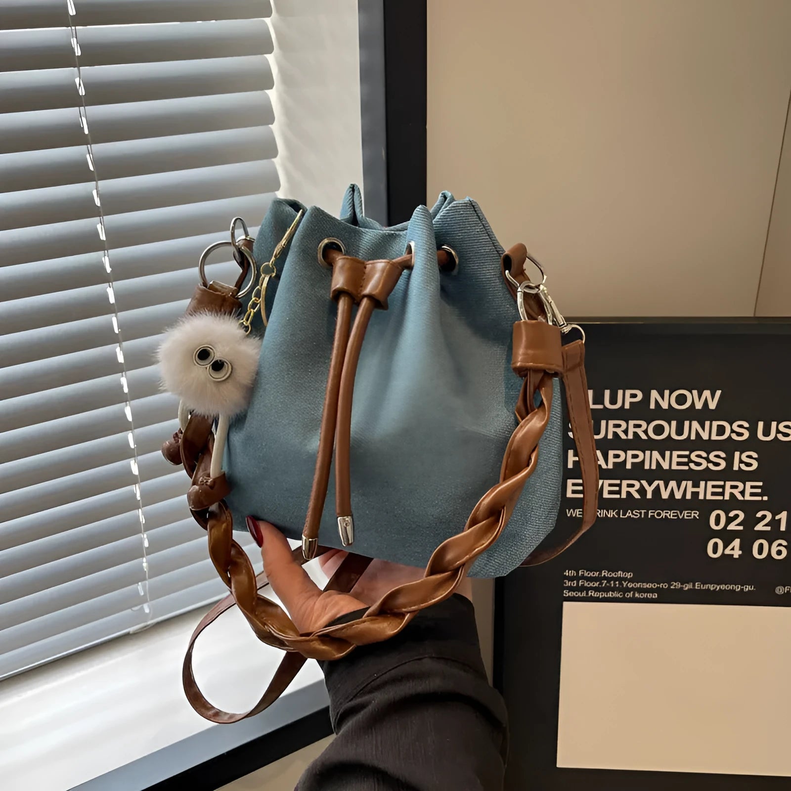 Blue one-shoulder cross body bucket bag with synthetic leather lining and hanging drop ornament