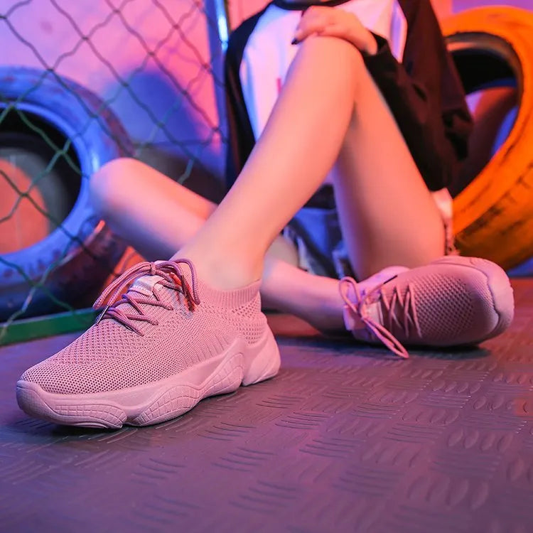 Women's white fly knit slip-on sport shoes with a thick rubber sole and front strap.