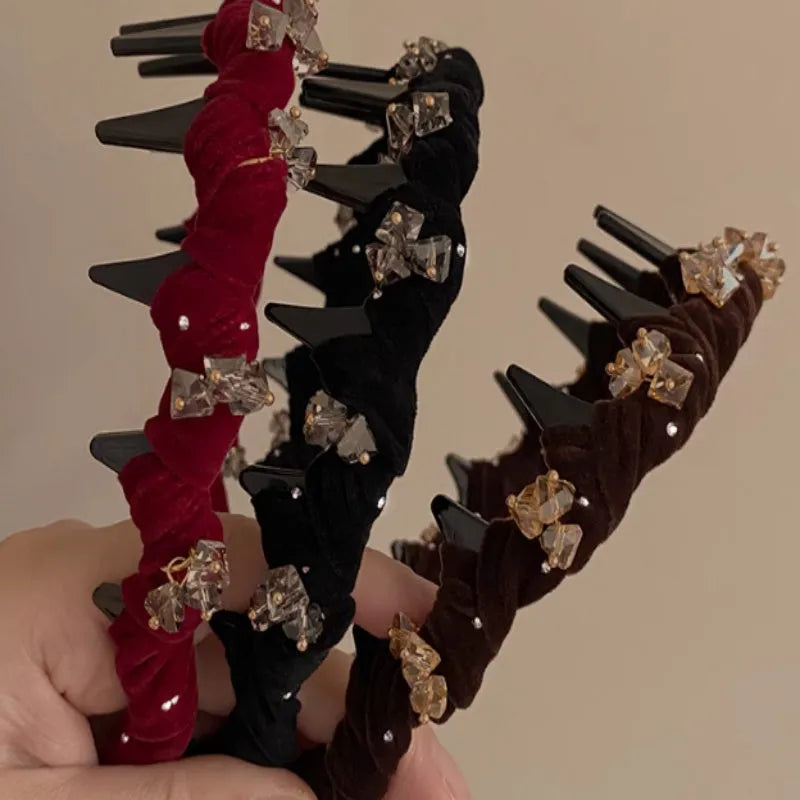 A wine red velvet hairband with a crystal wave decoration, sitting on a dark surface.