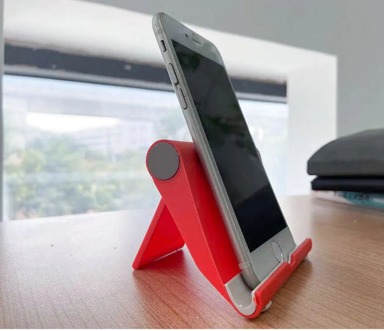 Black foldable PE plastic phone and tablet stand on a desktop, showing adjustable viewing angles.