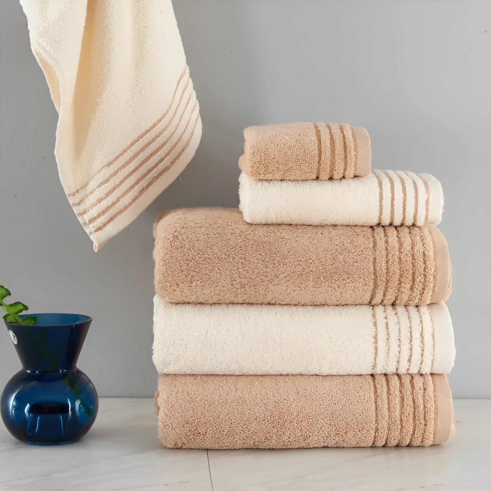 Beige and brown cotton towel set showing three sizes: square face cloth, hand towel, and bath towel.