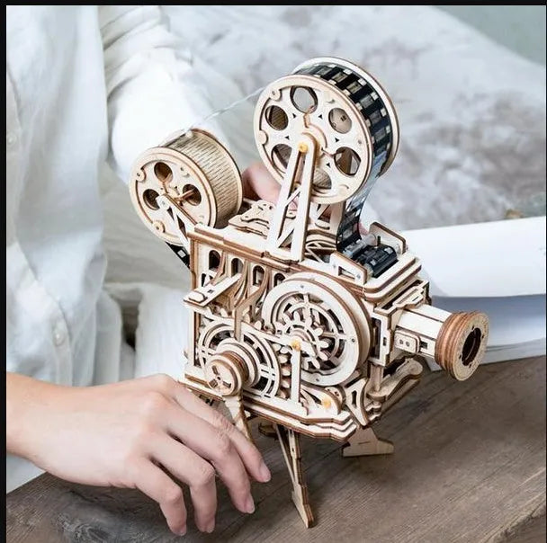 Flat-packed wooden 3D puzzle film projector with visible gear wheel assembly and hand crank