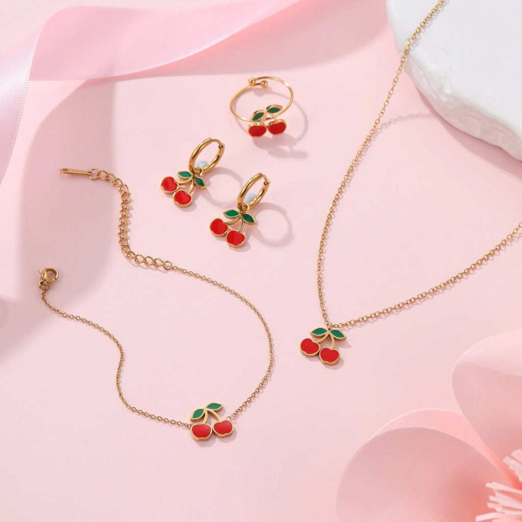 Cherry design jewellery set with gold plated necklace, bracelet, earrings, and ring on a flat surface.
