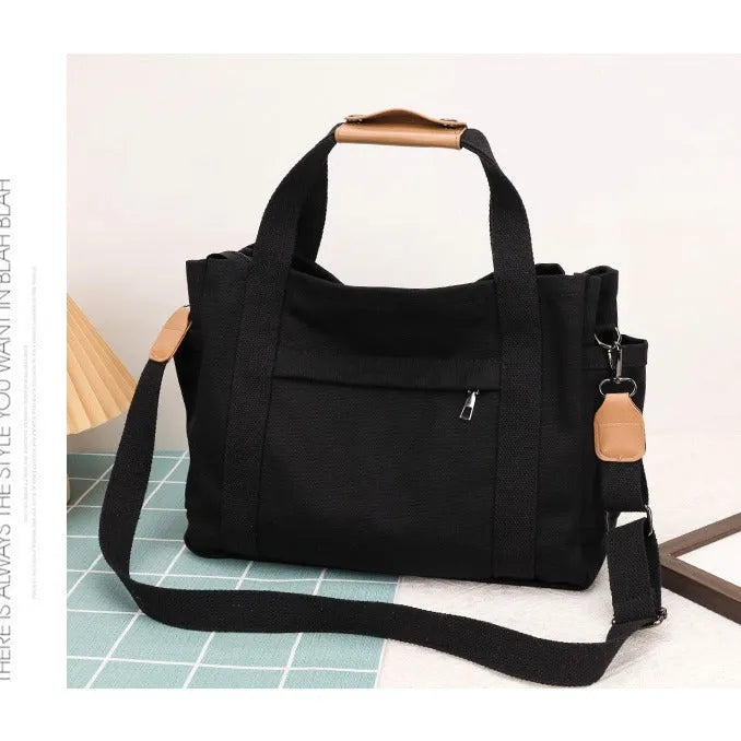 Horizontal square canvas tote bag in neutral colour with open zipper sides showing internal phone, document, computer and camera pockets