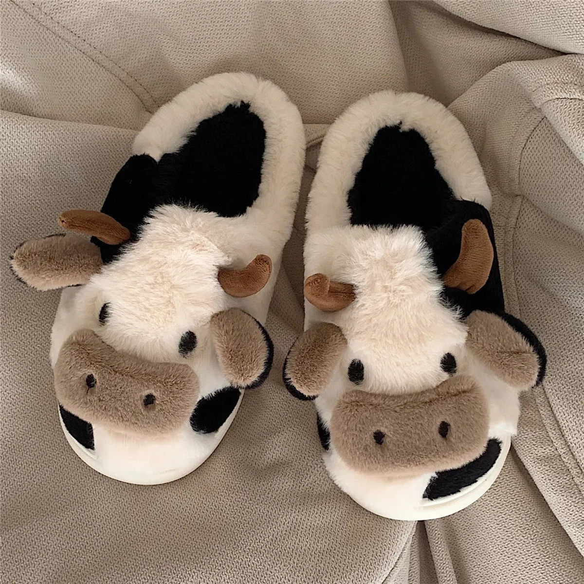 White cartoon cow slippers with plush faux fur and a textured non-slip sole.