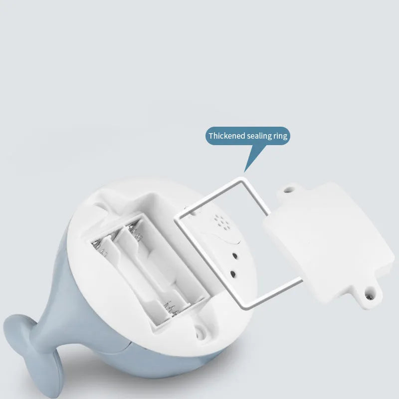 Automatic electric whale bath toy spraying water with LED lights on, floating in a baby bath.