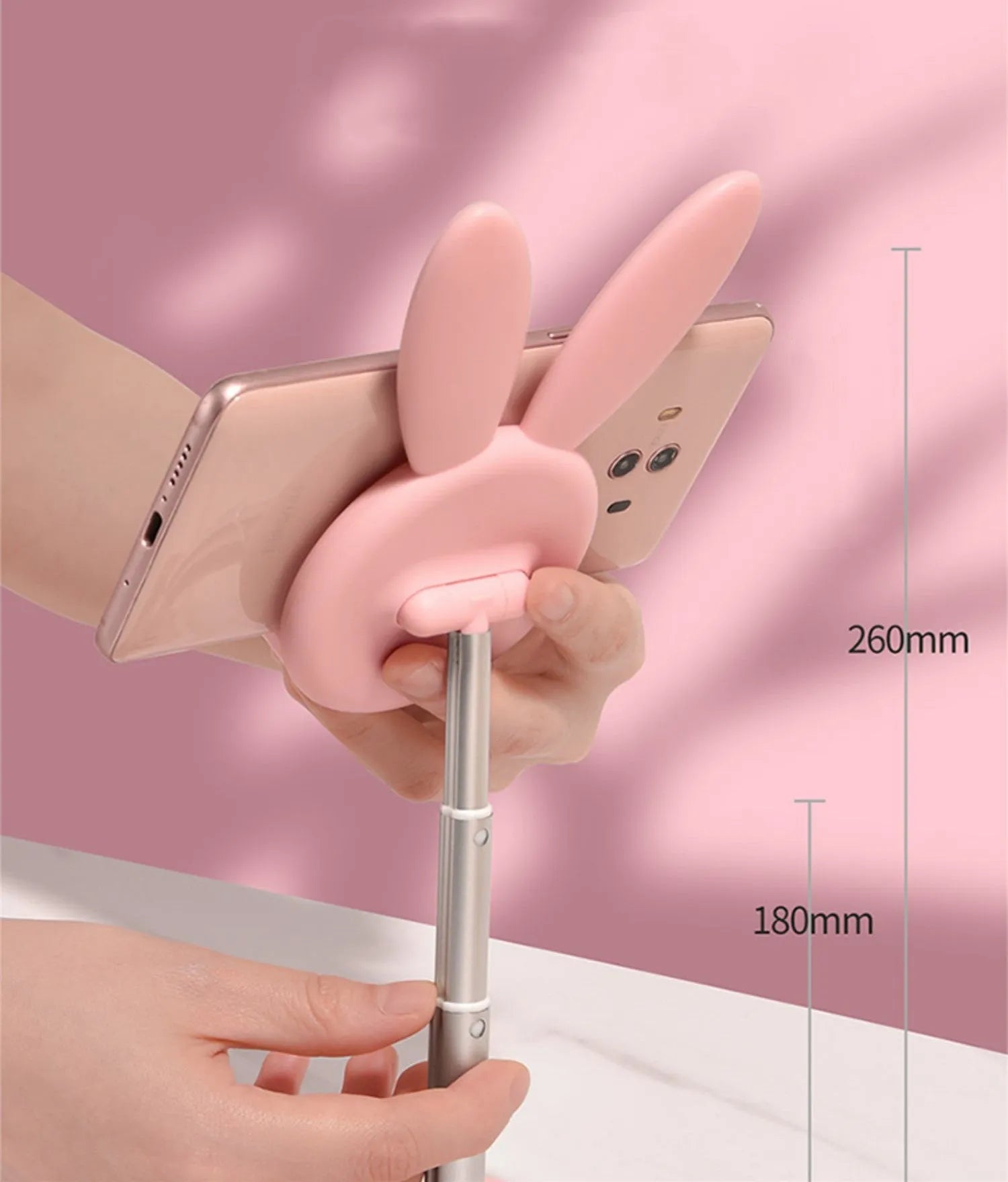 Silicone rabbit phone stand in pink on a desk holding a smartphone at an adjustable angle