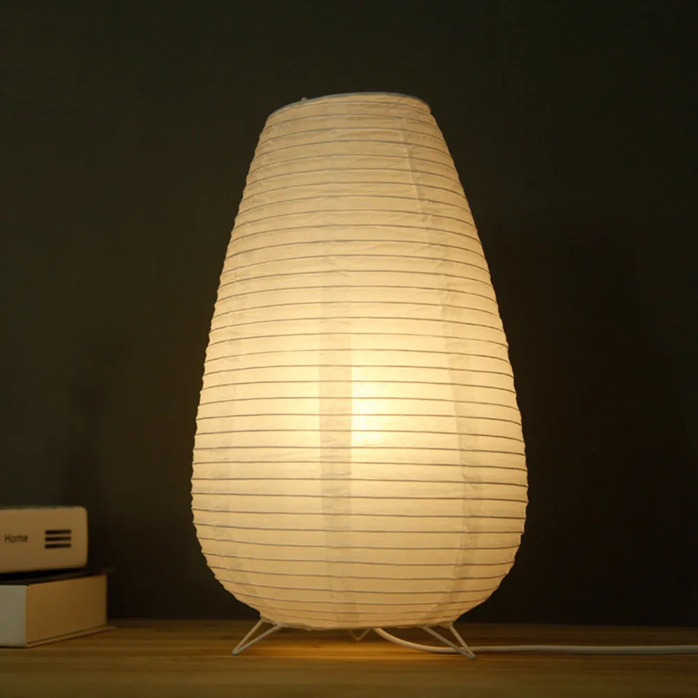 White rice paper plug-in table lamp in circular shape on a wooden bedside table.