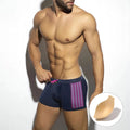 Men's black polka dot swimming boxers with a dark blue ribbon trim on a grey background.