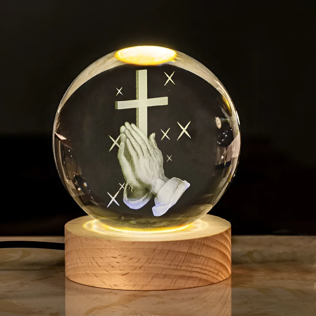 White crystal ball ornament on a wooden warm light base, showing engraved religious symbols.