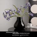 Black and white ceramic round belly french style decorative vase with two artificial flowers.