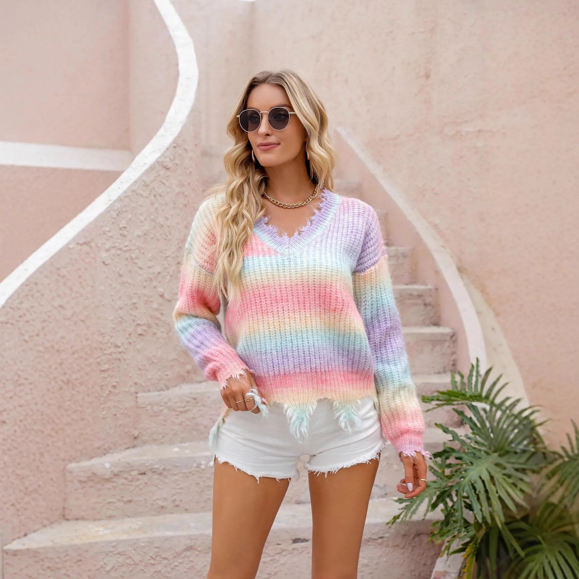 Pink rainbow gradient loose-cut knitted pullover sweater with tassels on a hanger.