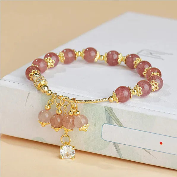 Close-up of a women's pink strawberry quartz crystal bracelet with heart-shaped beads and pearl accents.