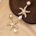 Women's gold-tone starfish drop earrings with a single off-white pearl centre on a light background