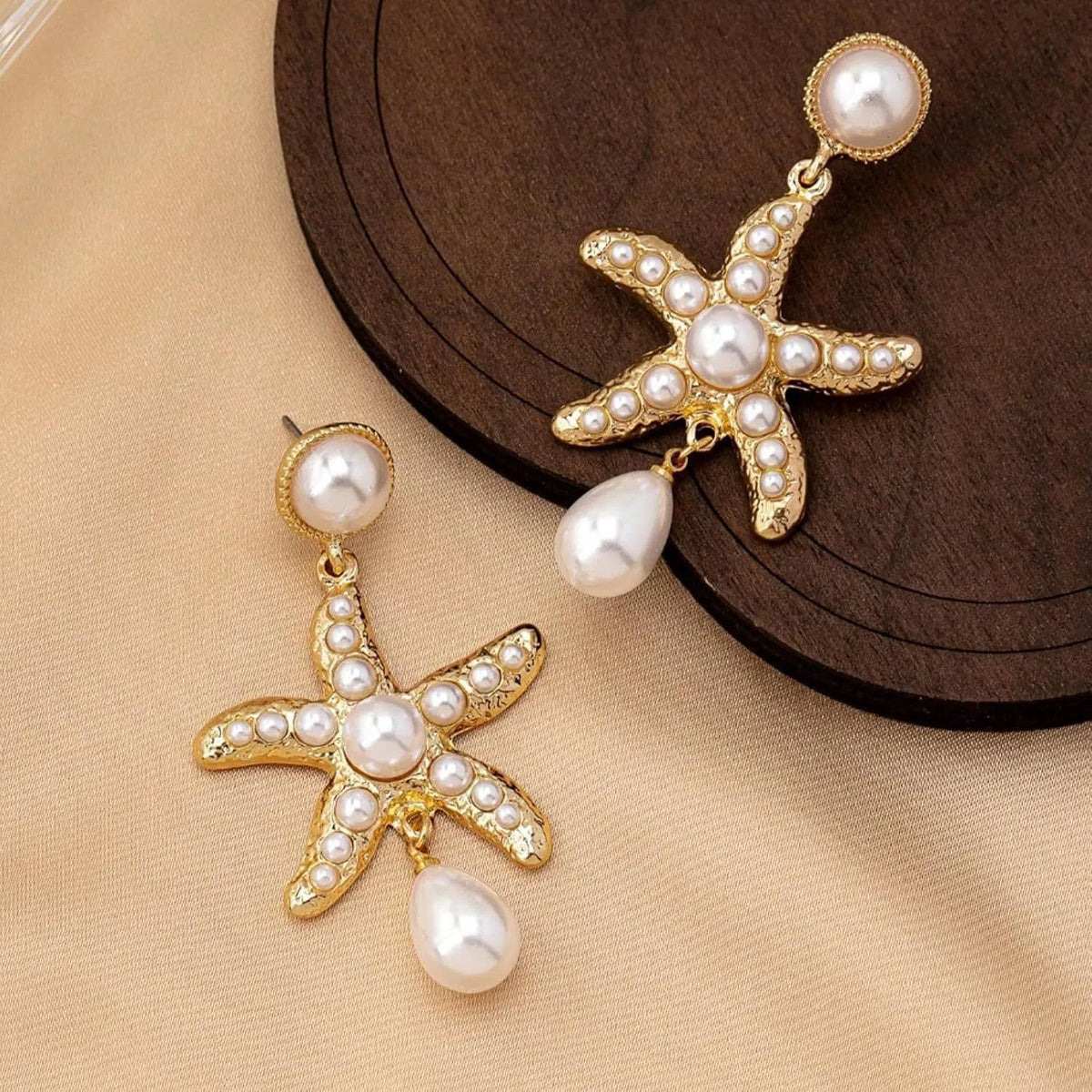 Women's gold-tone starfish drop earrings with a single off-white pearl centre on a light background